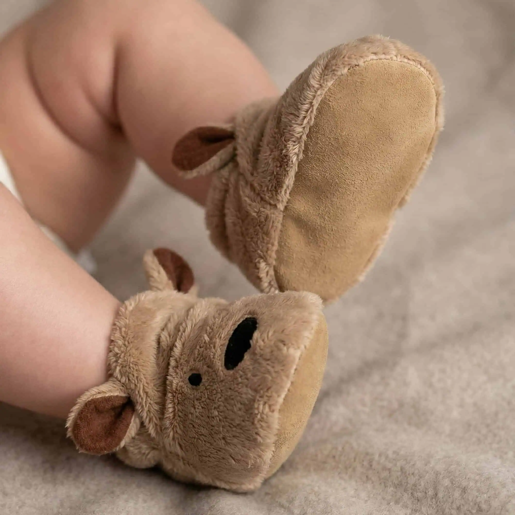 Brown bear baby booties by Funky Feet Fashions on an infant's feet, featuring plush ears and non-slip suede soles.